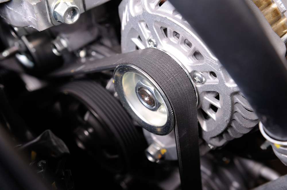 Close-up view of a car engine’s serpentine belt system, showing the black rubber belt looped tightly around several metallic pulleys and components, including the alternator. The polished metal surfaces and belt texture are in sharp focus, emphasizing the complexity of the engine’s mechanical design during a professional auto repair inspection in Clarke County.