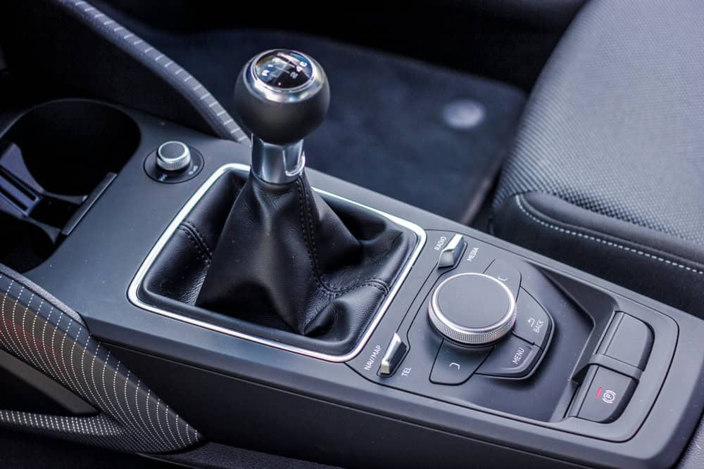 Close-up view of a car’s center console showcasing a manual gear shift wrapped in black leather with detailed stitching. Surrounding the gear shift are multiple control buttons and dials for vehicle functions. Part of the driver’s seat and a cup holder are also visible, highlighting the vehicle’s interior design and driver-focused layout, relevant for those seeking engine repair services in Clarke County.