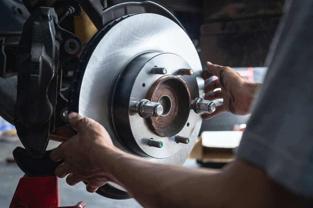 A mechanic's hands are working on a car’s braking system in Clarke County, carefully positioning or inspecting the brake rotor and caliper. The close-up view reveals detailed metal components, bolts, and the brake assembly during an auto repair procedure.