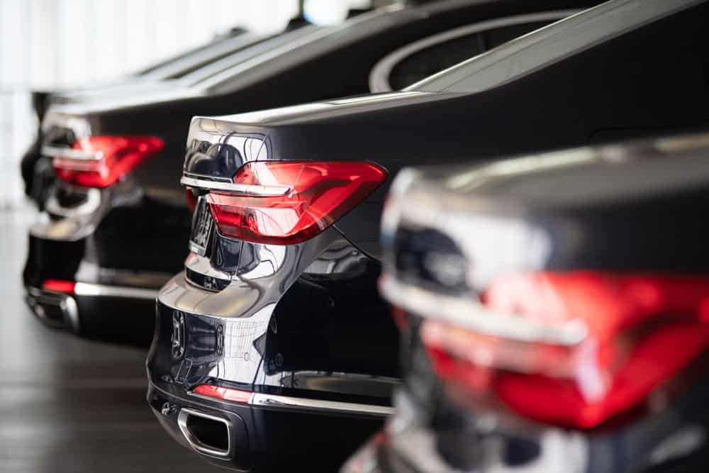 A close-up view of the rear ends and illuminated tail lights of several sleek black luxury cars, perfectly aligned in a clean, indoor automotive service bay. The glossy surfaces of the vehicles reflect soft ambient lighting, while the background is intentionally blurred, drawing focus to the precision and uniformity of the lineup—ideal representation of expert brake repair services in Clarke County.