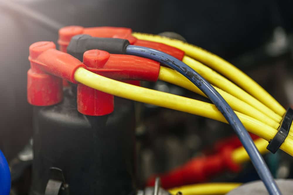 Close-up of colorful automotive ignition wires connected to a red distributor cap and ignition coil terminals. Yellow and blue wires are neatly bundled and firmly attached to their respective terminals, forming part of a vehicle's ignition system. The scene shows clean connections and precise routing, indicating recent inspection or repair by a professional mechanic in Clarke County.