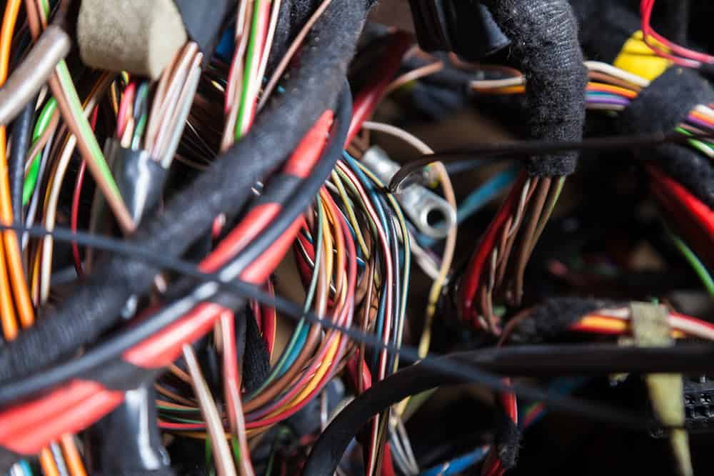 A close-up view of a densely packed bundle of colorful electrical wires—red, yellow, blue, green, and black—tangled and intertwined within a vehicle’s wiring harness. The wires are held together with black zip ties and beige plastic connectors, evoking the intricate complexity often seen during automotive electrical repairs in a Clarke County mechanic’s workshop.