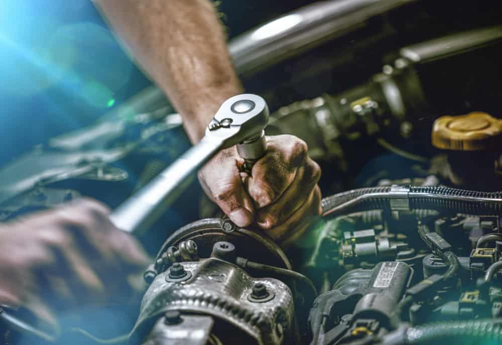 Close-up of a mechanic’s gloved hands using a wrench on a car engine, surrounded by various components. Bright lighting from the left highlights the tool and intricate engine parts, showcasing skilled workmanship typical of Engine Repair in Clarke County.