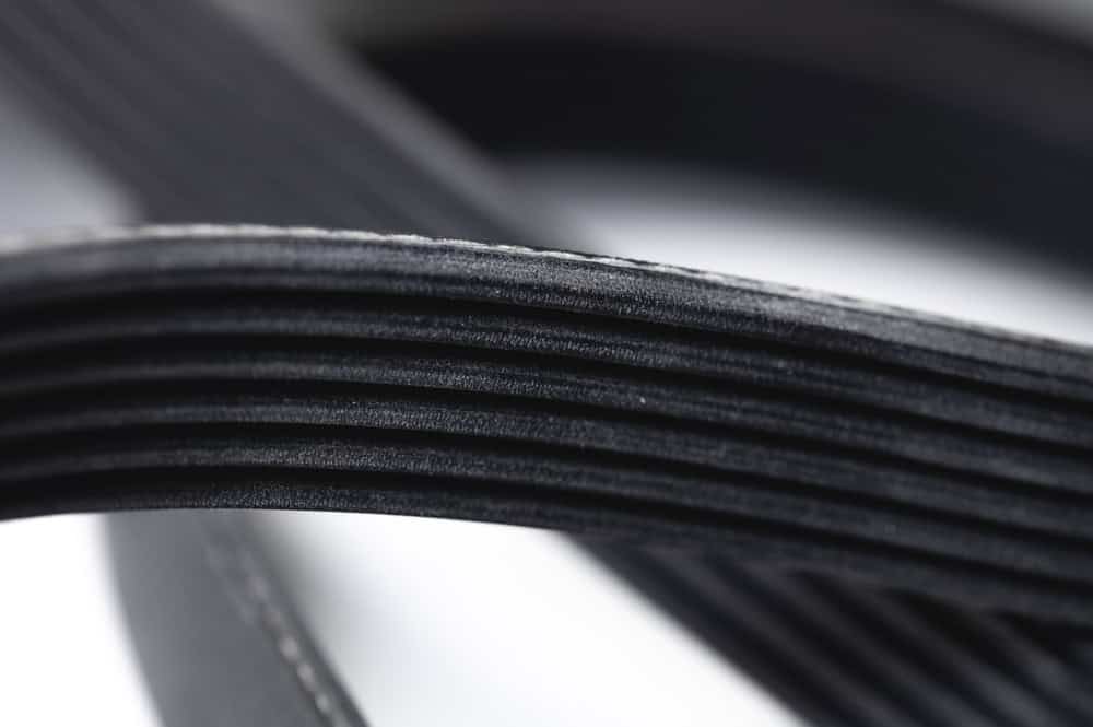 Close-up image of a black ribbed automotive belt, showing the detailed texture and grooves of the belt surface. The belt appears to be curved, creating a dynamic perspective and emphasizing its flexible material. Perfect representation of quality parts used in Auto Repair Clarke County services.