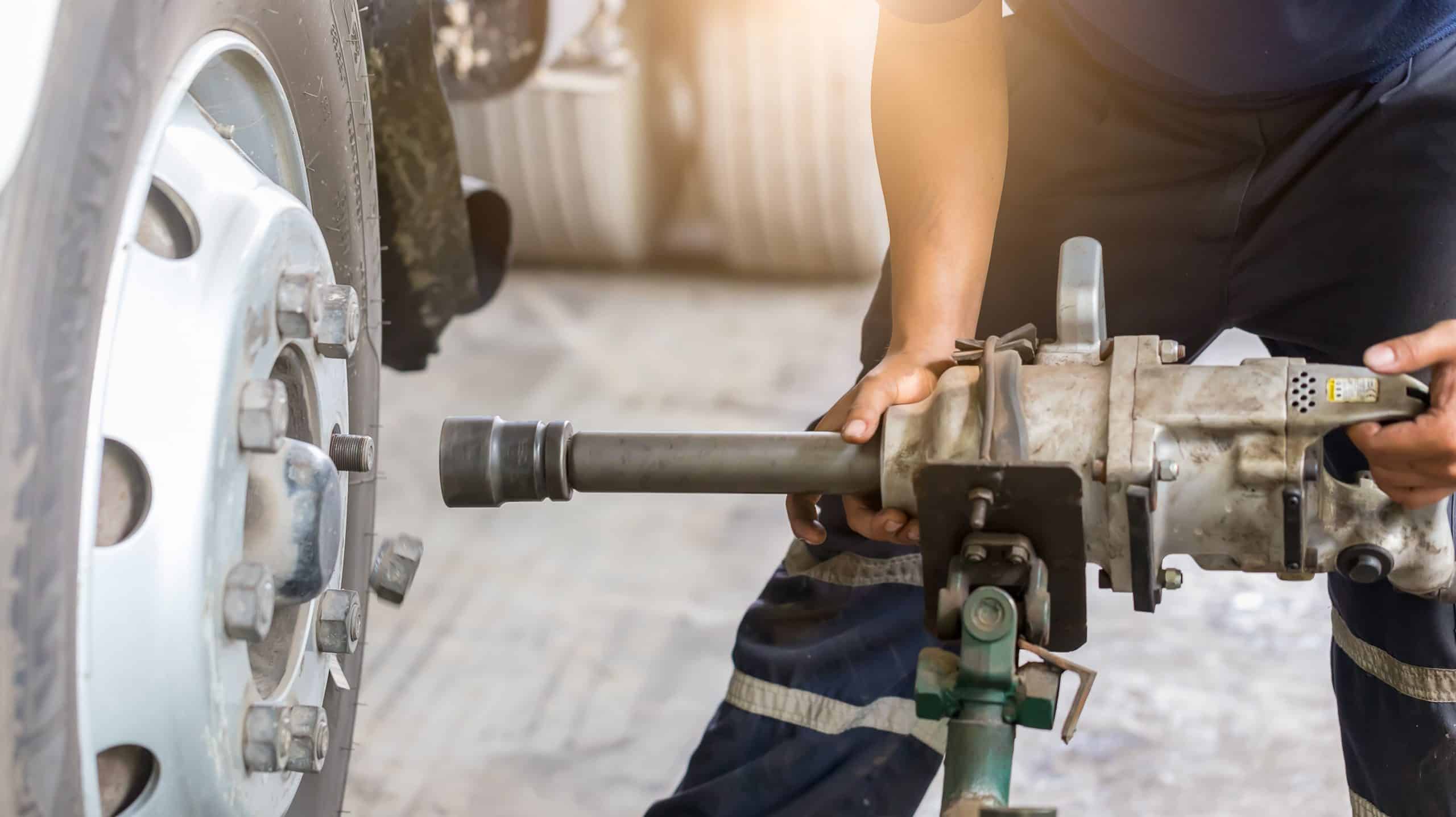 A person uses a pneumatic impact wrench connected to an air supply to remove a large lug nut from a truck wheel inside an auto repair shop in Clarke County. The individual’s gloved hands firmly guide the tool, emphasizing precision and expertise in heavy-duty vehicle maintenance.