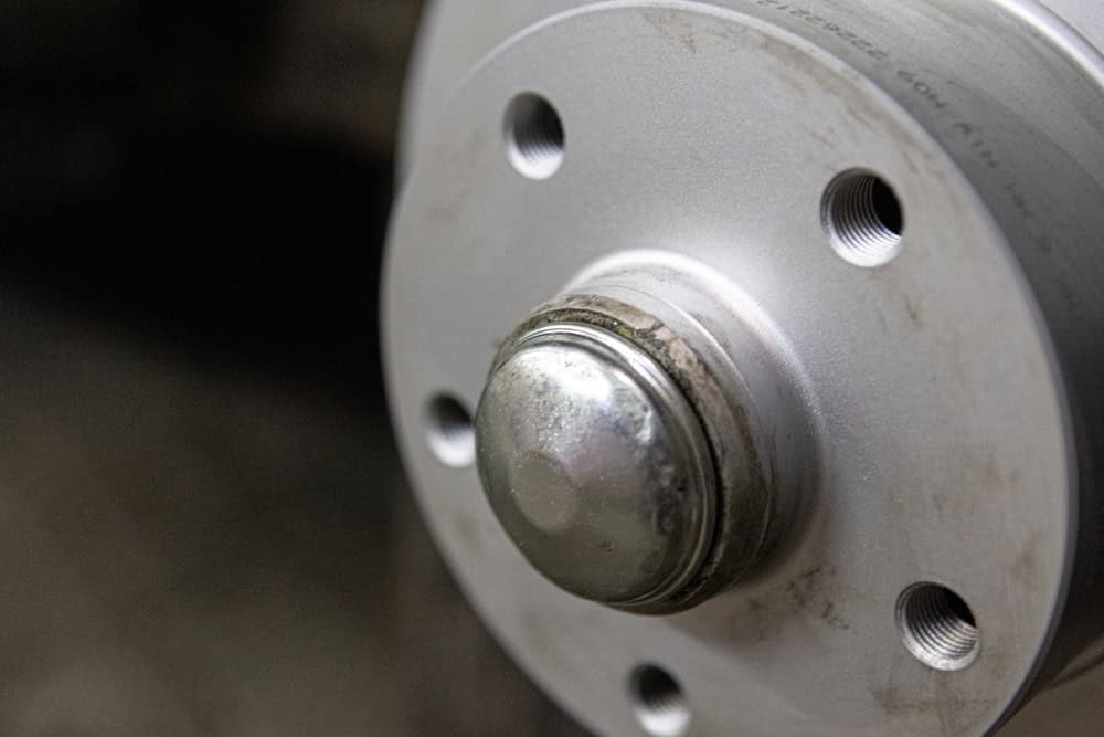 A close-up view of a car wheel hub, showing a silver metal finish. There are four bolt holes in the hub with a prominent center cap, which appears slightly worn. The background is blurred, keeping focus on the hub assembly. This image represents the precision required for auto repair in Clarke County.
