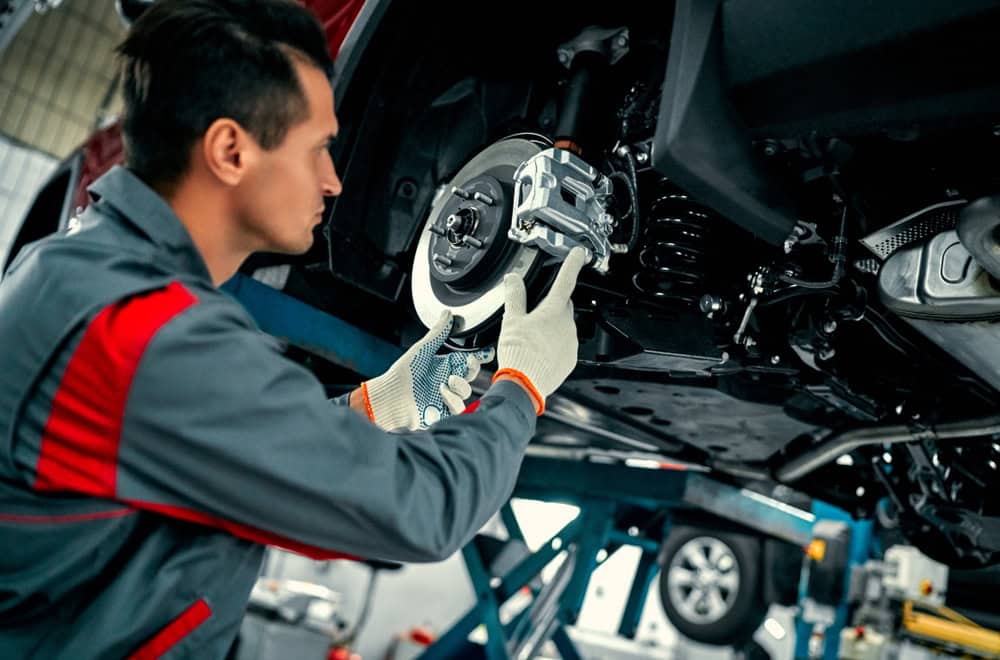 A mechanic wearing gloves inspects or repairs the brake system of a car lifted on a hydraulic lift in an auto repair shop in Athens, GA, known for expert transmission builds.