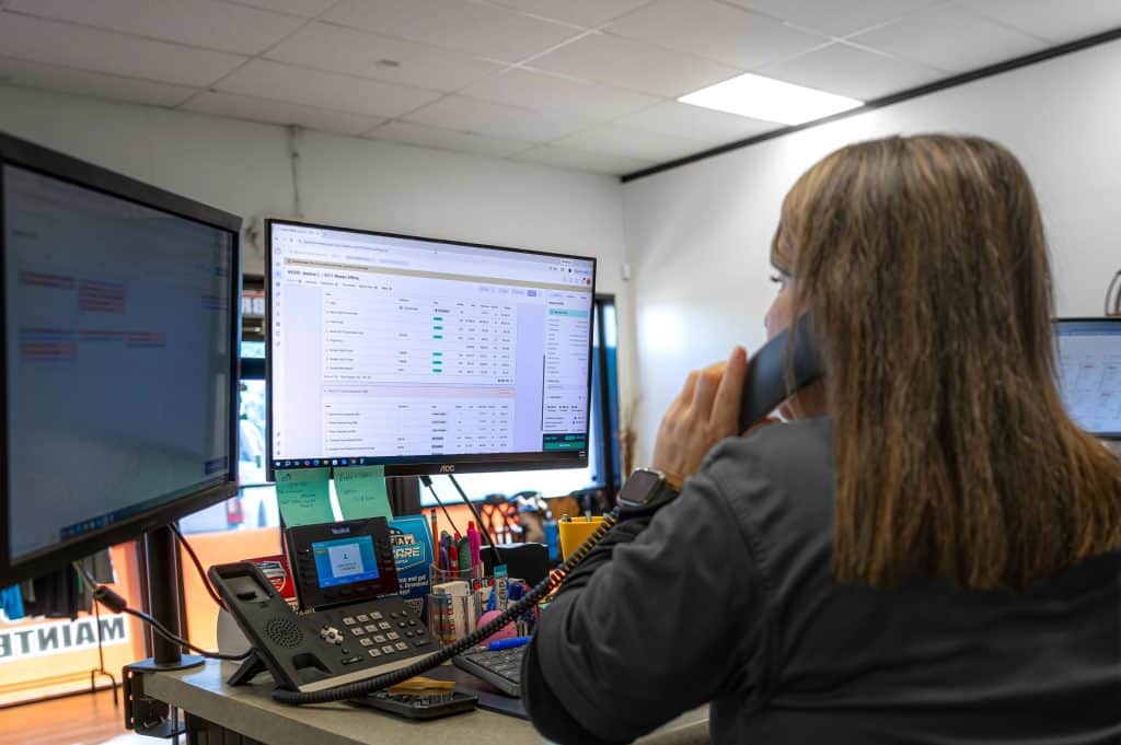 Desk employee talking into a corded landline phone whilst looking at a monitor.